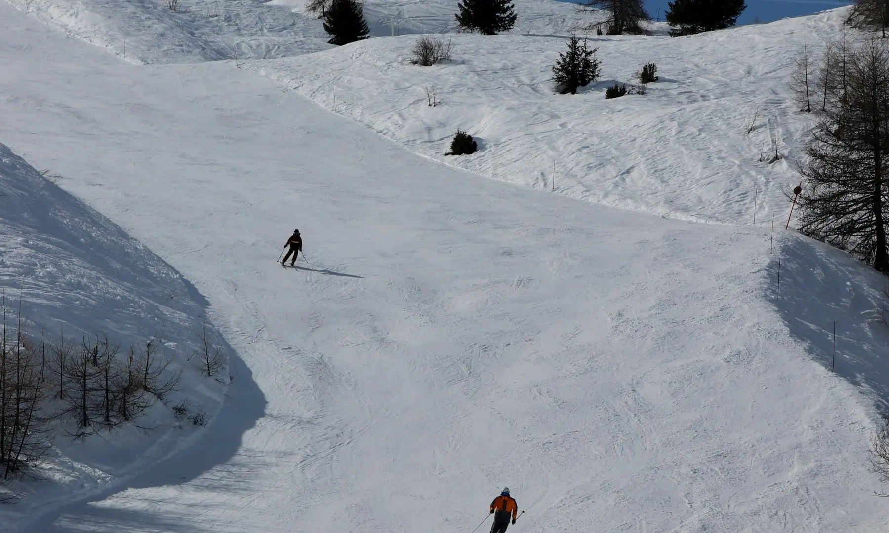 Two skiers carving down a groomed slope in the French Alps under a clear blue sky